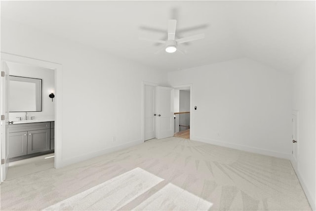 unfurnished bedroom featuring ensuite bathroom, baseboards, light colored carpet, ceiling fan, and vaulted ceiling