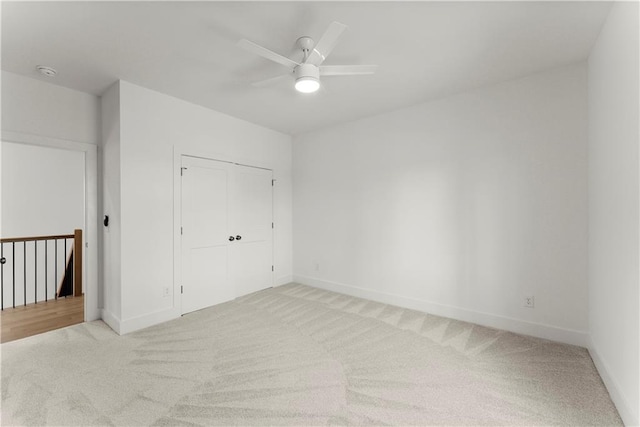 unfurnished bedroom featuring light carpet, ceiling fan, baseboards, and a closet