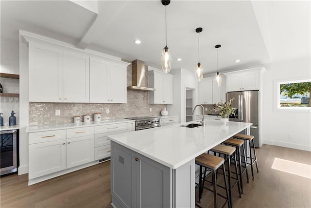 kitchen with a sink, wood finished floors, wine cooler, appliances with stainless steel finishes, and wall chimney range hood