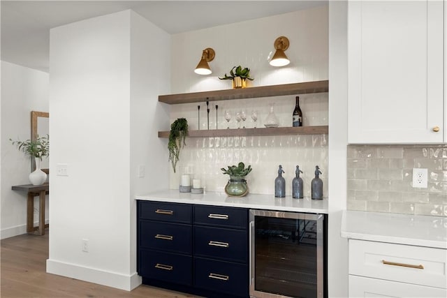 bar featuring wine cooler, backsplash, a bar, and light wood-style flooring