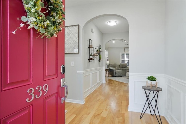 foyer featuring arched walkways, wainscoting, a decorative wall, and light wood finished floors