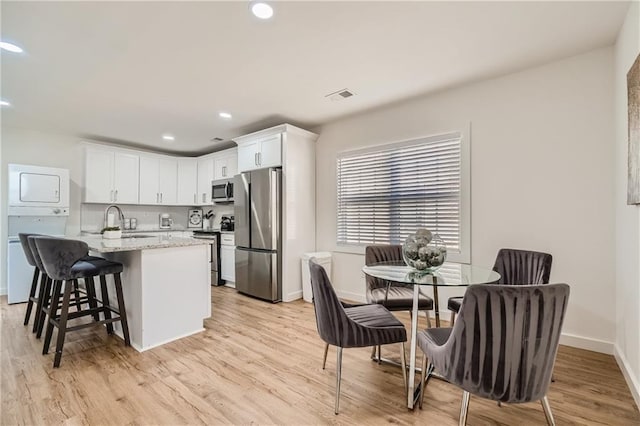 kitchen with sink, light wood-type flooring, appliances with stainless steel finishes, light stone countertops, and white cabinetry