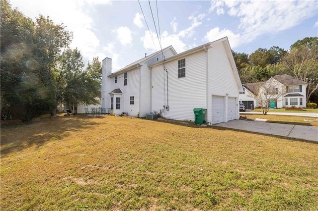 rear view of house with central AC unit, a garage, and a yard