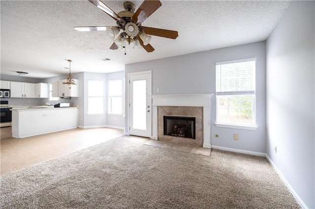 unfurnished living room featuring light colored carpet, a textured ceiling, ceiling fan, and a tile fireplace