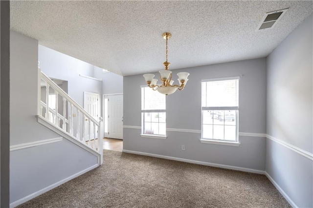 carpeted empty room featuring a textured ceiling and an inviting chandelier