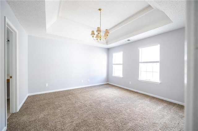 carpeted empty room with a textured ceiling, a chandelier, and a raised ceiling