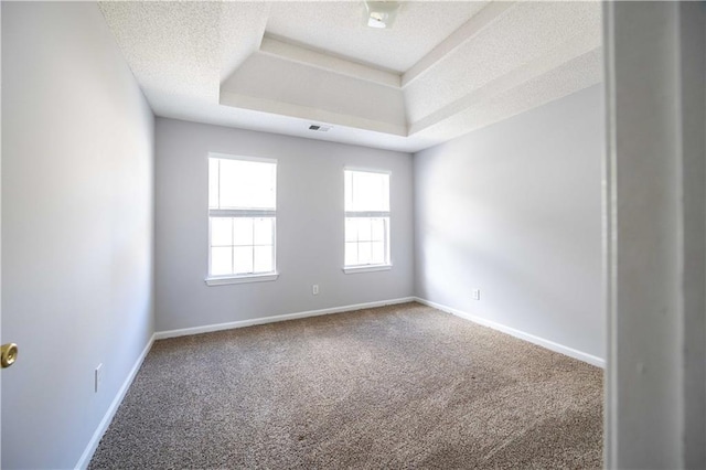 empty room with a tray ceiling, a textured ceiling, and carpet floors