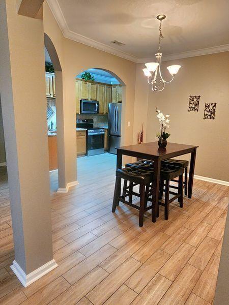 5449 Festival Ave, Fairburn, GA 30213 - dining area with arched walkways, a chandelier, light wood-style floors, ornamental molding, and baseboards