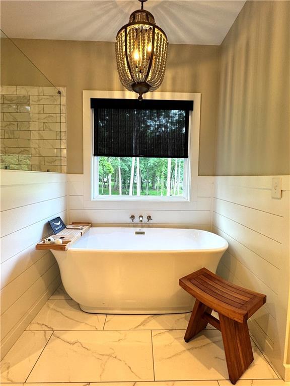 112 Three Oaks Dr SE, Calhoun, GA 30701 - bathroom featuring marble look tiles, a soaking tub, a chandelier, and wainscoting