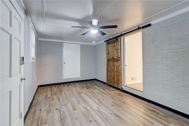 122 Vickery Dr, Fairburn, GA 30213 - unfurnished bedroom with brick wall, wood finished floors, baseboards, a barn door, and a ceiling fan
