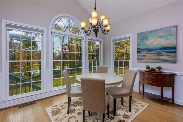 dining area with a chandelier, vaulted ceiling, and light hardwood / wood-style flooring