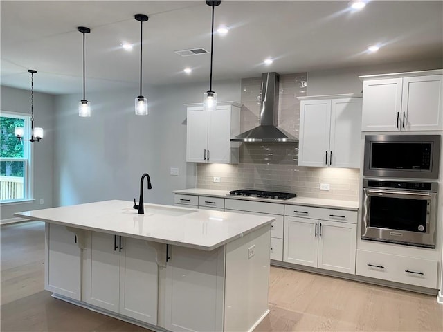 7206 Grand Reunion Dr, Hoschton, GA 30548 - kitchen with appliances with stainless steel finishes, wall chimney range hood, backsplash, white cabinetry, and a center island with sink