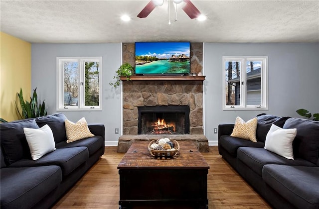 living room with hardwood / wood-style floors, ceiling fan, a stone fireplace, and a textured ceiling