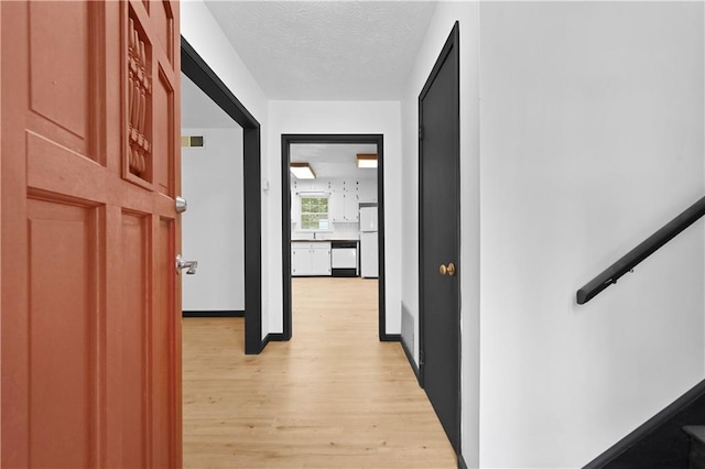 corridor with light wood-style floors, visible vents, and a textured ceiling