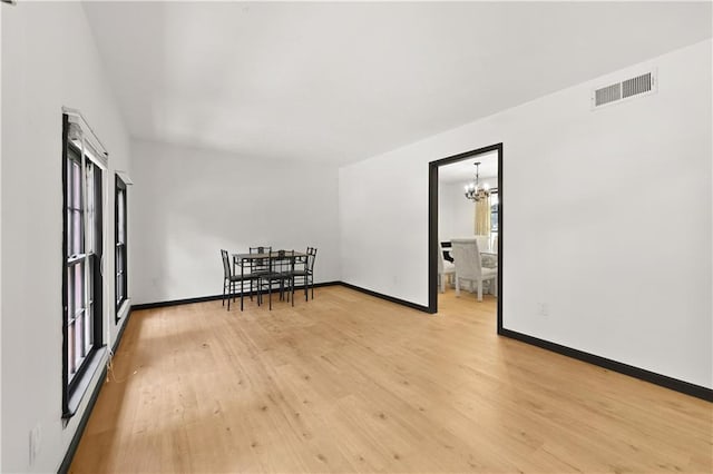 unfurnished room with visible vents, light wood-style flooring, baseboards, and an inviting chandelier