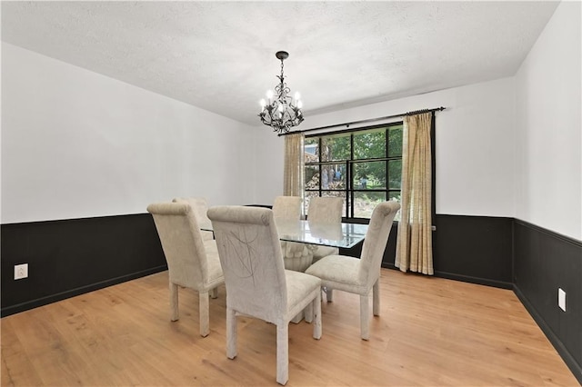 dining area with wainscoting, light wood finished floors, and an inviting chandelier