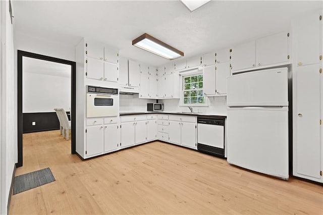 kitchen featuring white appliances, light wood finished floors, white cabinets, under cabinet range hood, and a sink