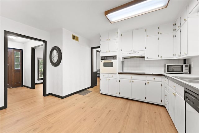 kitchen with white appliances, visible vents, under cabinet range hood, white cabinetry, and backsplash