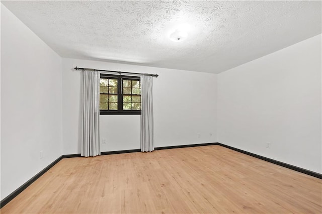 spare room with light wood-type flooring, baseboards, and a textured ceiling