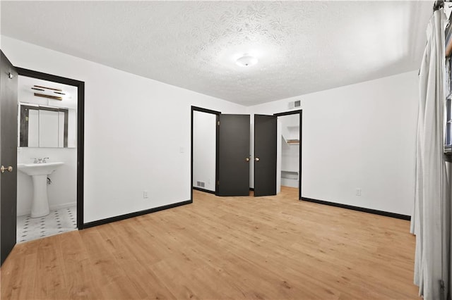 unfurnished bedroom with visible vents, light wood-style flooring, baseboards, and a textured ceiling