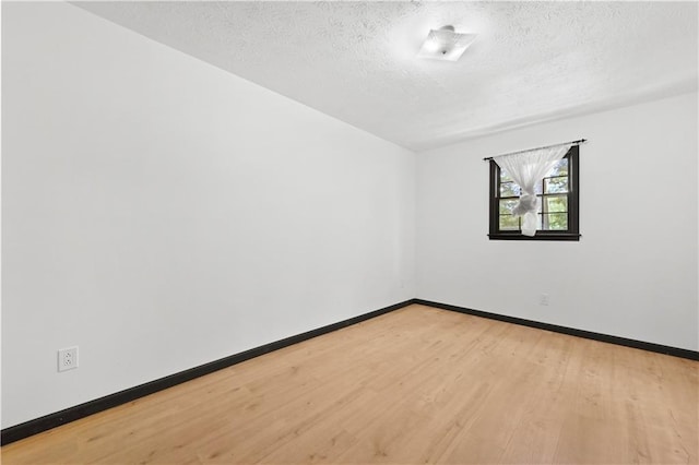 empty room with light wood-style flooring, baseboards, and a textured ceiling