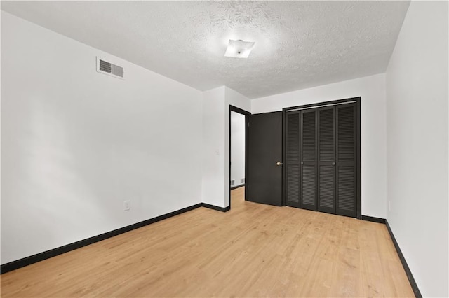 unfurnished bedroom featuring visible vents, a textured ceiling, baseboards, and wood finished floors