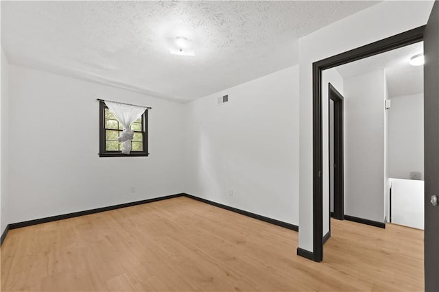 spare room featuring light wood-style floors, baseboards, visible vents, and a textured ceiling