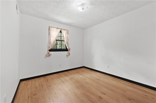 spare room featuring visible vents, a textured ceiling, baseboards, and wood finished floors