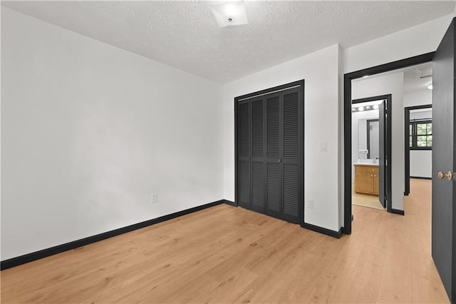 unfurnished bedroom with light wood-style floors, a closet, a textured ceiling, and baseboards