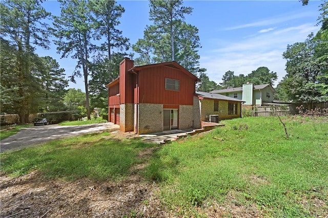 view of side of home featuring brick siding, a chimney, fence, a garage, and driveway