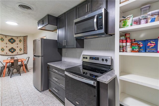 kitchen featuring stainless steel appliances, a textured ceiling, light tile patterned floors, and decorative backsplash