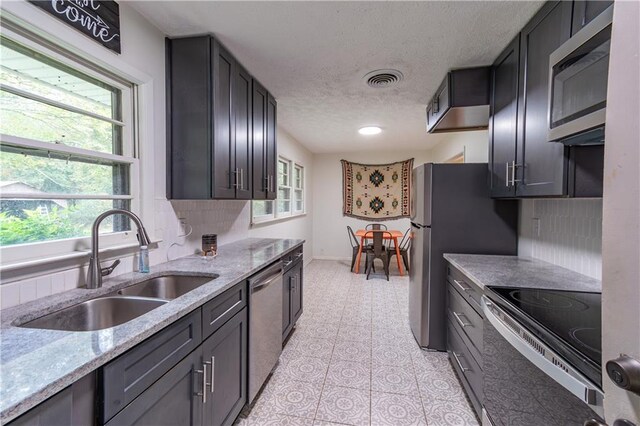 kitchen with decorative backsplash, stainless steel appliances, sink, and light stone counters