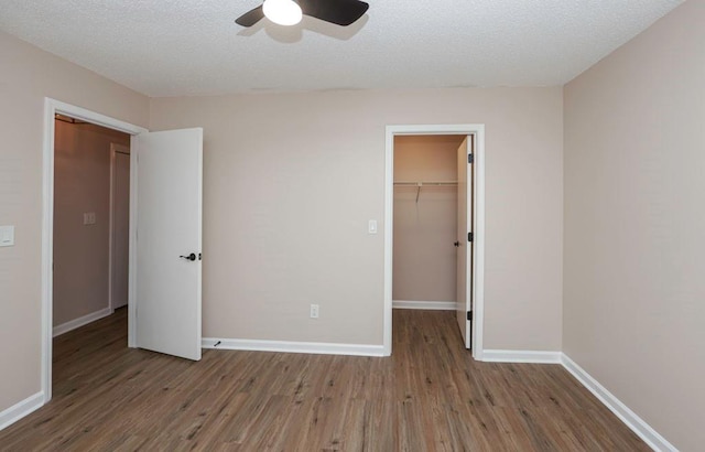 unfurnished bedroom with a walk in closet, light wood-type flooring, a textured ceiling, ceiling fan, and a closet