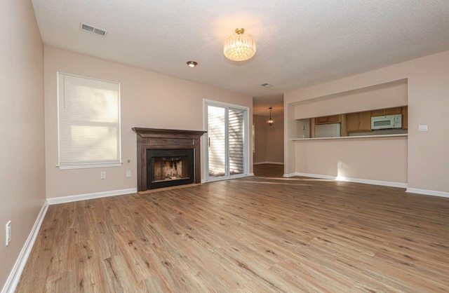 unfurnished living room with light hardwood / wood-style floors, a textured ceiling, and a notable chandelier