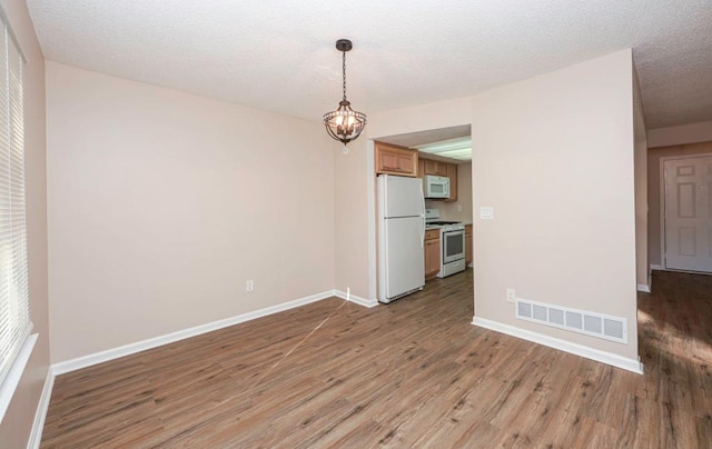 empty room featuring light wood-type flooring, a textured ceiling, and a chandelier