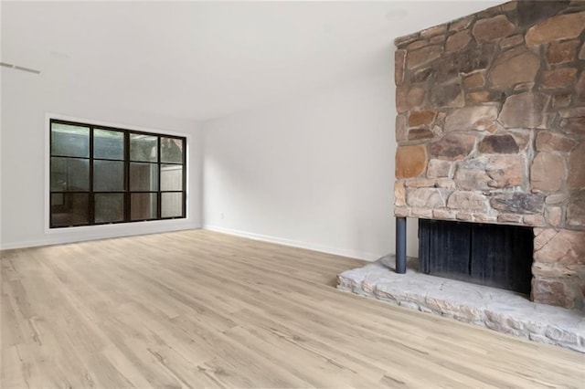 unfurnished living room featuring a stone fireplace, wood finished floors, and baseboards