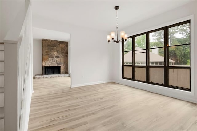 unfurnished dining area featuring wood finished floors, a chandelier, baseboards, and a fireplace