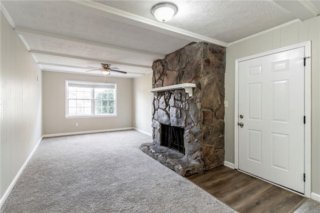 unfurnished living room with ceiling fan, a stone fireplace, dark hardwood / wood-style floors, a textured ceiling, and ornamental molding