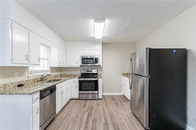 kitchen featuring sink, light hardwood / wood-style flooring, light stone counters, white cabinetry, and stainless steel appliances