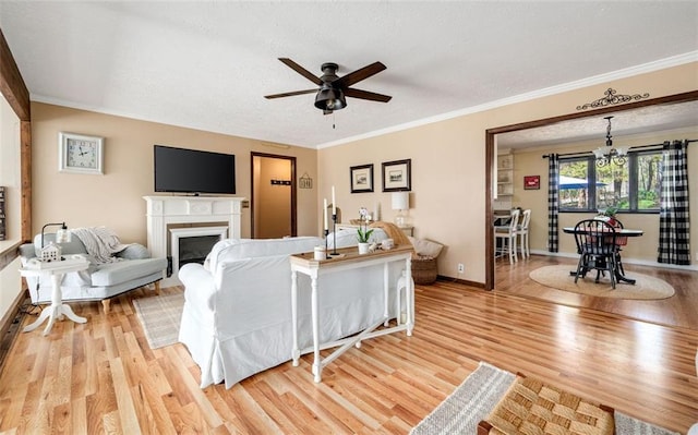 living area with baseboards, ornamental molding, light wood-type flooring, a fireplace, and ceiling fan with notable chandelier