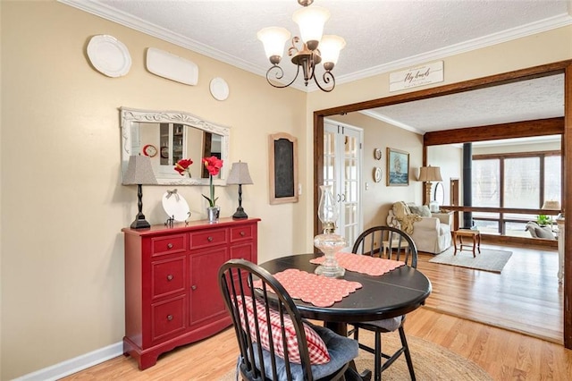 dining space with light wood-type flooring, a chandelier, a textured ceiling, and ornamental molding