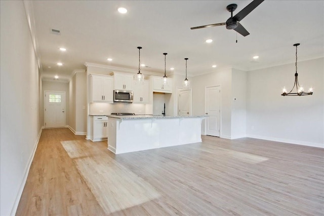 kitchen with light wood-type flooring, ceiling fan with notable chandelier, pendant lighting, a center island with sink, and white cabinetry