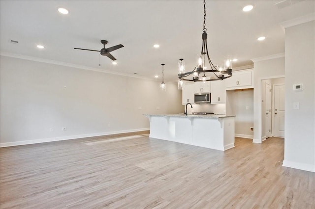 kitchen with white cabinetry, light stone counters, pendant lighting, a kitchen island with sink, and ceiling fan with notable chandelier