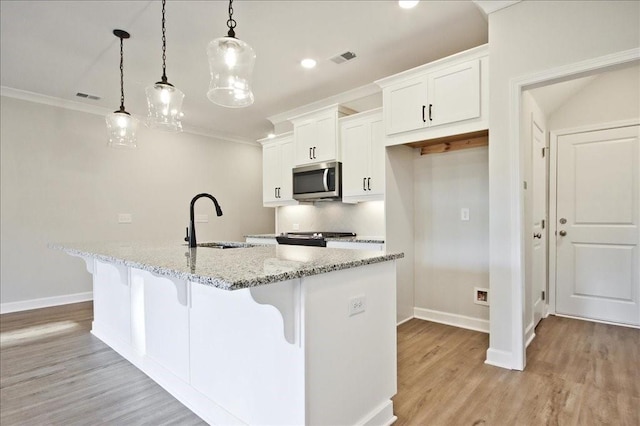 kitchen with decorative light fixtures, light stone countertops, sink, and an island with sink