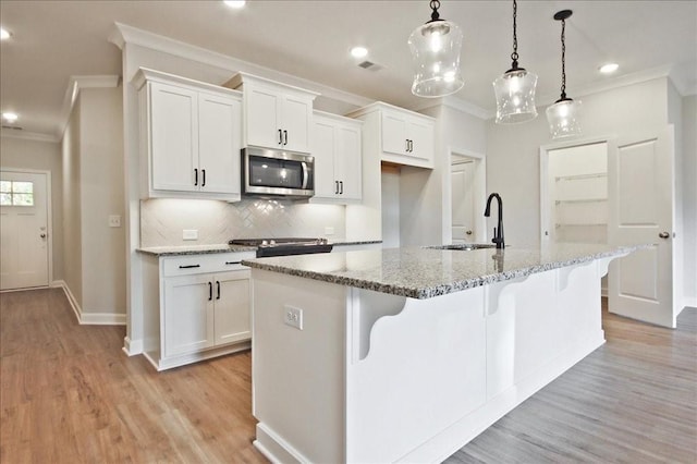 kitchen with a kitchen island with sink, white cabinets, sink, light stone countertops, and decorative light fixtures