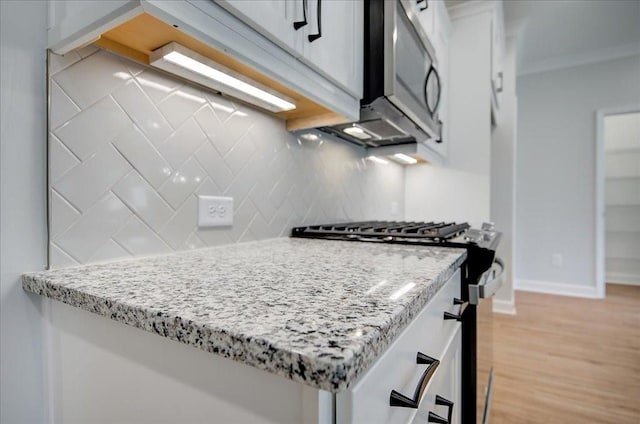 kitchen with white cabinets, light stone countertops, stainless steel range with gas cooktop, and tasteful backsplash