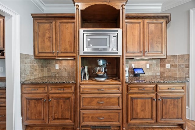 2517 Stone Manor Dr, Buford, GA 30519 - kitchen featuring stainless steel microwave, dark stone countertops, decorative backsplash, ornamental molding, and brown cabinetry