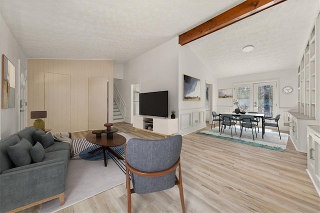 living area with stairway, vaulted ceiling with beams, a textured ceiling, french doors, and light wood-type flooring