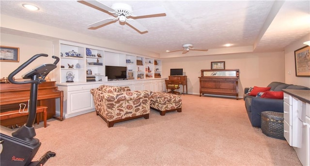 living room featuring light carpet, a textured ceiling, a tray ceiling, and ceiling fan