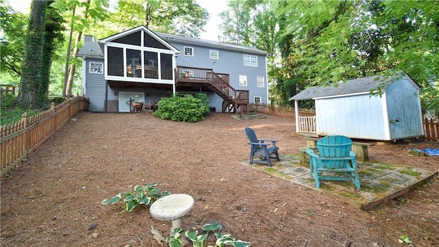 back of house with a sunroom, a wooden deck, a fire pit, a storage shed, and a patio area